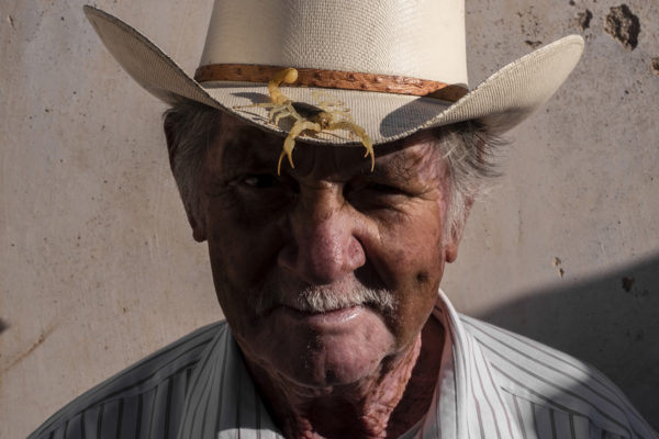 An old man poses with a blonde scorpion on his cowboy hat (alacrán güero).